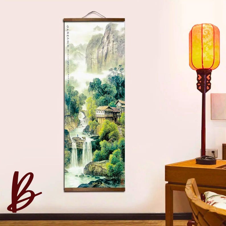 May include: A vertical wall hanging featuring a watercolor painting of a mountain landscape with waterfalls, trees, and buildings. The artwork is framed with wooden rods and a hanging cord. The color palette includes greens, blues, and browns.