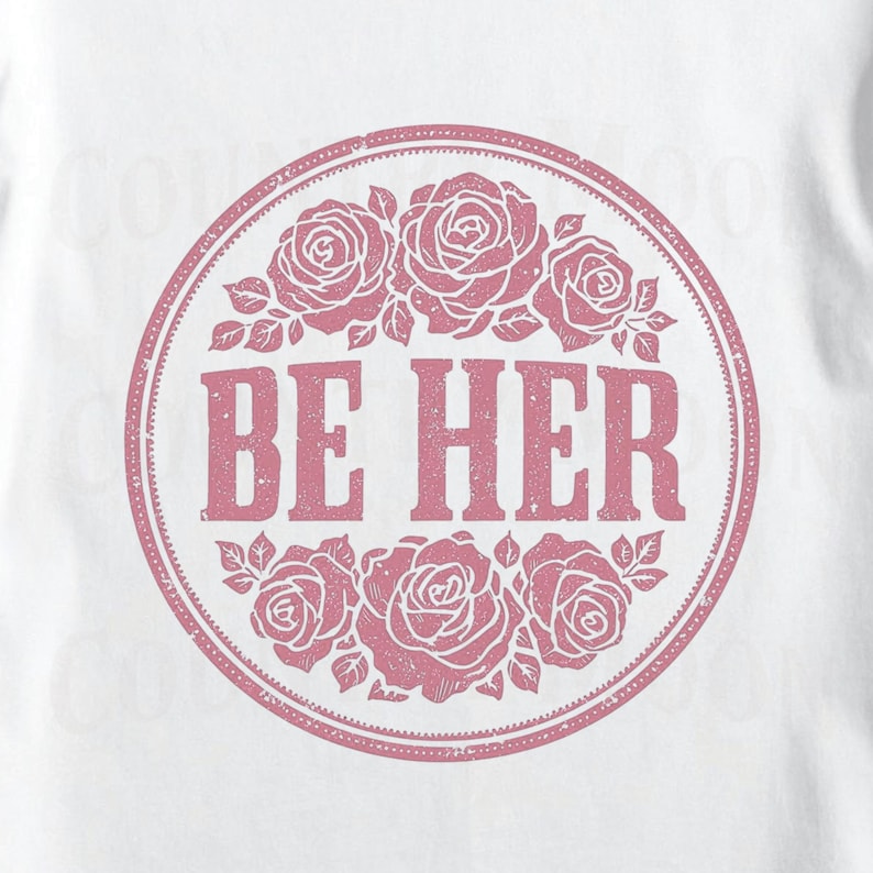 May include: White t-shirt featuring a circular design with the text "BE HER" in a distressed font. The design is surrounded by a ring of pink roses and leaves, creating a floral and feminine aesthetic.