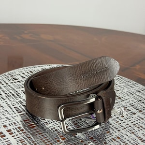 May include: A brown leather belt with a silver-colored buckle. The belt is rolled up and has the brand name "DUNSHILL" embossed on the leather. The belt is on a white patterned surface.