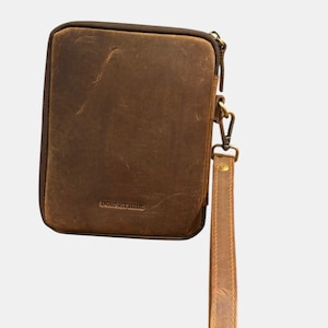 May include: A rectangular brown leather zippered pouch with a distressed finish and a detachable wrist strap. The brand name DORSET HIDE is embossed in the lower center of the front panel. The pouch features a dark brown zipper and metal hardware.