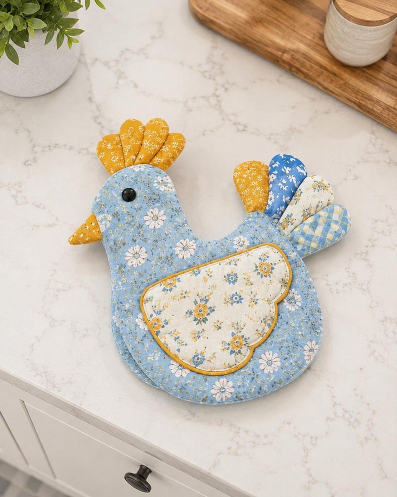 May include: A fabric chicken-shaped pot holder featuring a light blue base with a white daisy floral pattern. It has a yellow patterned comb and beak, a black eye, and a cream-colored wing with blue and yellow flowers. The tail feathers are multicolored.