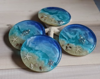 Puede incluir: Cuatro posavasos redondos de resina azul y blanca con temática de playa. Cada posavasos presenta una criatura marina diferente, incluyendo una estrella de mar, una tortuga y un pulpo. Los posavasos son perfectos para agregar un toque de encanto costero a la decoración de tu hogar.