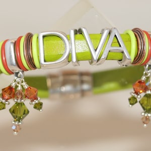 May include: A green leather bracelet with the word "DIVA" in silver lettering. The bracelet has multiple layers of red, orange, and copper colored beads. The bracelet has two dangling charms with green and orange crystals.