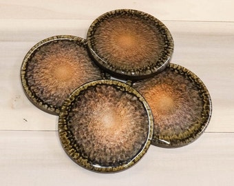 Puede incluir: Cuatro posavasos redondos con un diseño marmoleado marrón y dorado. Los posavasos tienen un anillo exterior marrón oscuro con un anillo interior marrón más claro. El centro de cada posavasos es de color dorado claro.