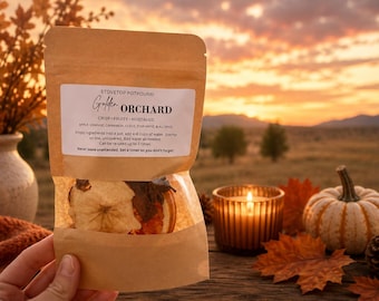 May include: A brown paper pouch of stovetop potpourri labeled Golden Orchard. The label lists ingredients including apple, orange, cinnamon, clove, star anise, and allspice. The clear bottom window reveals dried fruit slices and spices inside the bag.