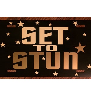 May include: A black license plate with gold stars and the text "SET TO STUN" in gold letters.