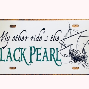 Puede incluir: Placa de matrícula de metal blanco con texto negro que dice "My other ride's the BLACK PEARL" y una ilustración en blanco y negro de un barco con velas.