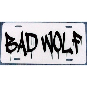 May include: White license plate with black graffiti-style lettering that reads "BAD WOLF".