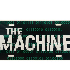 May include: A black license plate with white text that reads "THE MACHINE" in a pixelated font. The background of the plate is covered in a green binary code.
