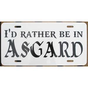 May include: White metal license plate with black text that reads "I'd rather be in Asgard".