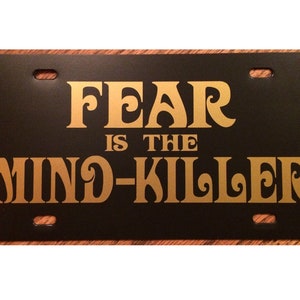 May include: Black license plate with gold lettering that reads "FEAR IS THE MIND-KILLER".