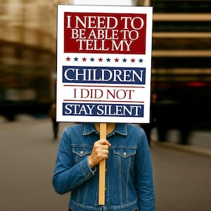 May include: A person holding a sign with the text "I NEED TO BE ABLE TO TELL MY CHILDREN I DID NOT STAY SILENT". The sign has a red and white color scheme with blue stars and text.