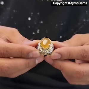 Peut inclure: Une bague en argent ornée d'une pierre précieuse ovale jaune. La bague présente un motif filigrané orné autour de la pierre et du corps. L'image comprend le texte "Copyright @AymaGems".