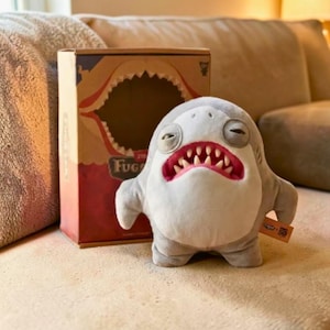 Op de afbeelding: Een set van drie keramische mokken met een gespikkelde, matte afwerking. De mokken zijn in crème, lichtgrijs en donkergrijs. Elke mok heeft een eenvoudig, minimalistisch ontwerp.