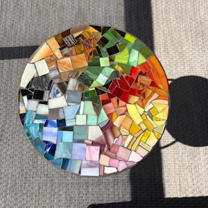 May include: A circular mosaic table top featuring a rainbow pattern of colourful glass tiles. The tiles are arranged in a swirling pattern, creating a vibrant and eye-catching design.