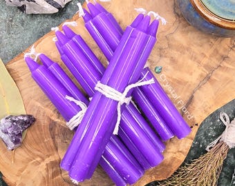 May include: A bundle of purple taper candles tied together with twine. The candles are on a wooden surface.