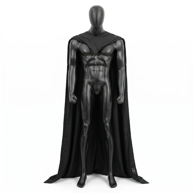 May include: A black floor-length cape draped over a featureless black mannequin. The cape features a structured collar that wraps around the shoulders and chest, with fabric extending down the back and sides to the floor in a solid black color.