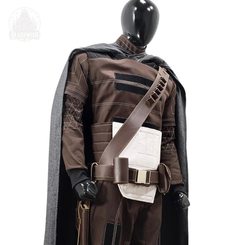 May include: A brown and black costume set featuring a long grey cape, a brown jacket with white paneling, and a brown utility belt with pouches. The outfit includes a diagonal shoulder strap with ammunition loops and black accents throughout.