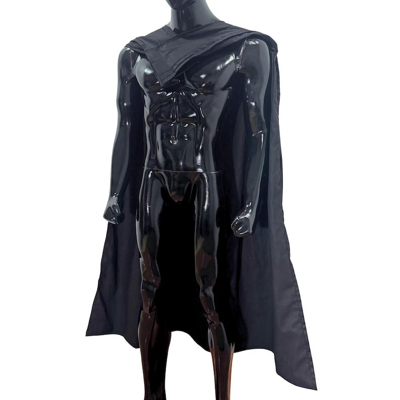 May include: A solid black cape draped over the shoulders of a glossy black mannequin. The cape features a simple, unadorned design with a straight hemline that falls down the back, covering the shoulders and extending to the lower torso area.