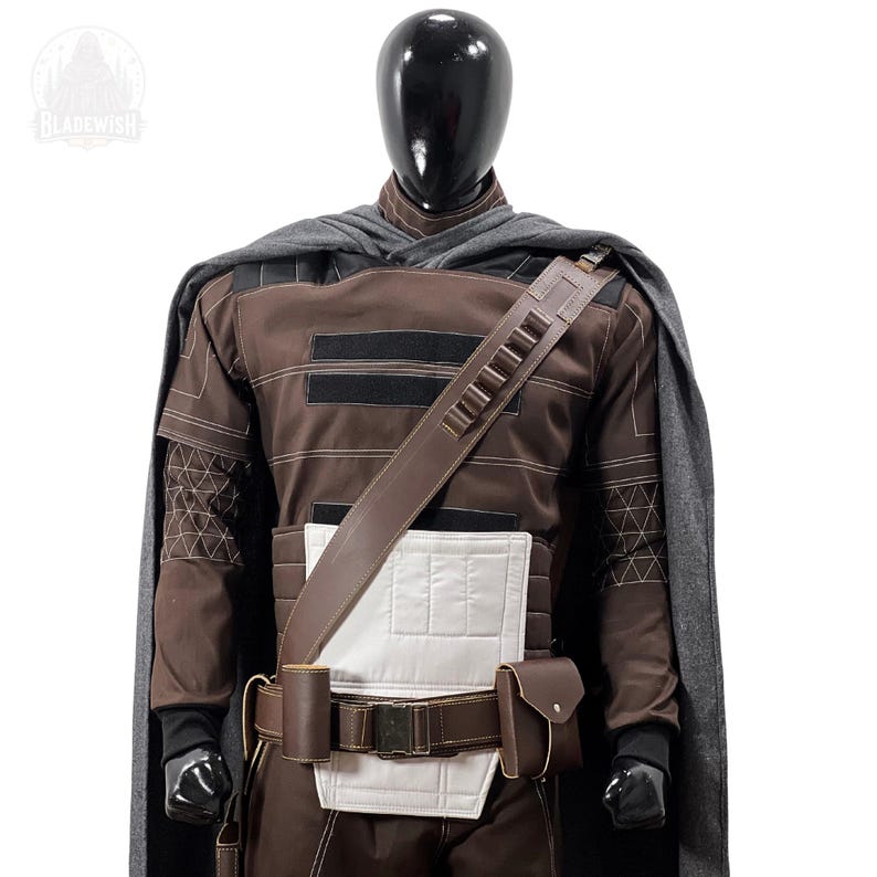 May include: A brown long-sleeved tunic with a white chest panel, a grey cape, and a brown utility belt featuring a diagonal shoulder strap with ammunition loops. The outfit is displayed on a black mannequin with a logo reading BLADEWISH.