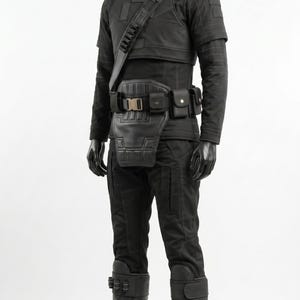 May include: A black tactical outfit displayed on a mannequin, featuring a high-neck shirt, structured vest, utility belt with multiple pouches, and a diagonal shoulder strap. The ensemble includes matching black trousers and tall, reinforced boots.