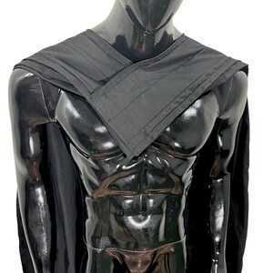 May include: A black cape featuring a structured, layered collar design that wraps across the chest. The garment is made of a solid black fabric with visible stitching along the edges of the collar and shoulder panels, draping over the shoulders.