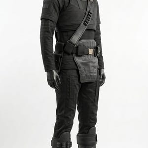 May include: A black tactical costume set worn on a mannequin, featuring a high-neck long-sleeve shirt, structured chest armor, a utility belt with a drop-down panel, and knee-high boots with integrated straps and decorative metallic hardware accents.