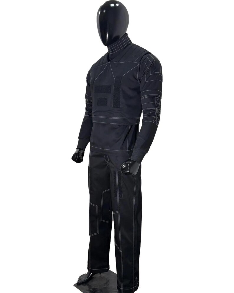 May include: A black long-sleeved top and matching trousers set featuring a high neck collar and white contrast stitching. The garment includes geometric paneling, rectangular patches on the chest, and reinforced stitching patterns on the sleeves.