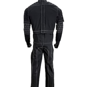 May include: A black long-sleeved jacket and matching trousers set featuring prominent white contrast stitching. The jacket includes a high collar, padded shoulder panels, and geometric triangular patterns on the sleeves. The trousers feature vertical seams.