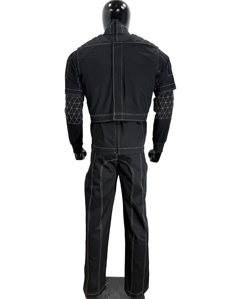 May include: A black long-sleeved jacket and matching trousers set featuring prominent white contrast stitching. The jacket includes a high collar, padded shoulder panels, and geometric triangular patterns on the sleeves. The trousers feature vertical seams.