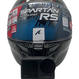 Könnte beinhalten: Ein schwarzer Shark Spartan RS Motorradhelm mit klarem Visier, blauen und roten Grafikakzenten, ECE 22/06 Zertifizierung und QR-Code. Eine schwarze DJI Action 4 Kamera ist mit einer Kunststoffhalterung am vorderen Kinnbereich befestigt.
