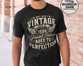 May include: Black t-shirt with the text "I'M NOT OLD I'M VINTAGE - MADE IN - 1996 - Limited Edition - AGED TO PERFECTION". The design includes wings and stars. The shirt is worn by a person.