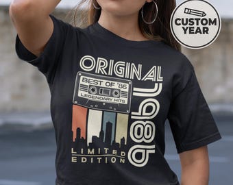 May include: Black t-shirt with a retro design featuring the text "ORIGINAL 1986" and a cassette tape graphic. The graphic includes the words "BEST OF '86" and "LEGENDARY HITS". Below the cassette tape is a skyline graphic and the words "LIMITED EDITION".
