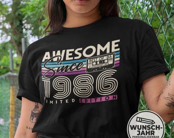 May include: A black short-sleeve t-shirt featuring a graphic print with the text AWESOME Since 1986 LIMITED EDITION and an illustration of a cassette tape labeled BEST OF '86 A LEGENDARY HITS, accented by horizontal teal, purple, and white stripes.