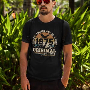 Puede incluir: Camiseta negra con un gr&aacute;fico circular que presenta el a&ntilde;o "1975", monta&ntilde;as y las palabras "Limited Edition - One of a Kind", "Original" y "Vintage". La camiseta tiene cuello redondo y mangas cortas.