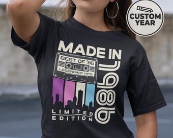 May include: Black t-shirt with a retro design featuring the text "MADE IN '86" and a cassette tape graphic. The design includes the words "BEST OF '86" and "LEGENDARY HITS". Below the tape is a skyline graphic with the words "LIMITED EDITION".