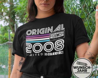 May include: Black t-shirt with the text "ORIGINAL 2008 LIMITED EDITION" in white. The design includes a retro cassette tape graphic and a horizontal stripe design in purple, pink, and teal. A white baseball cap is worn.