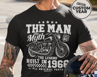 May include: Black t-shirt with a motorcycle graphic and the text "THE MAN THE MYTH THE LEGEND BUILT IN 1966". The design includes Route 66 and the words "ALL ORIGINAL PARTS (MOSTLY)". A custom year option is available.