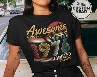 May include: A black short-sleeve t-shirt featuring a graphic print with the text Awesome since 1976 Limited Edition. The design includes a sunset with palm tree silhouettes and horizontal stripes in yellow, orange, red, and teal colors.