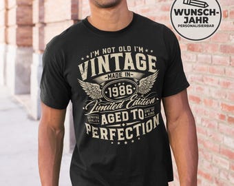 May include: Black t-shirt with a vintage design. The shirt features the text "I'M NOT OLD I'M VINTAGE MADE IN 1986 Limited Edition AGED TO PERFECTION". A round graphic on the upper right says "WUNSCH-JAHR PERSONALISIERBAR".