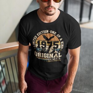 Puede incluir: Camiseta negra con un dise&ntilde;o vintage que presenta el a&ntilde;o "1975", monta&ntilde;as y un &aacute;guila. La camiseta tiene el texto "Limited Edition - One of a Kind" y "Original Vintage Aged to Perfection".