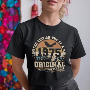 Puede incluir: Camiseta negra con un dise&ntilde;o vintage que presenta el a&ntilde;o "1975". El dise&ntilde;o incluye un &aacute;guila, monta&ntilde;as y las palabras "Limited Edition - One of a Kind" y "Original". La camiseta tiene un cuello redondo cl&aacute;sico.