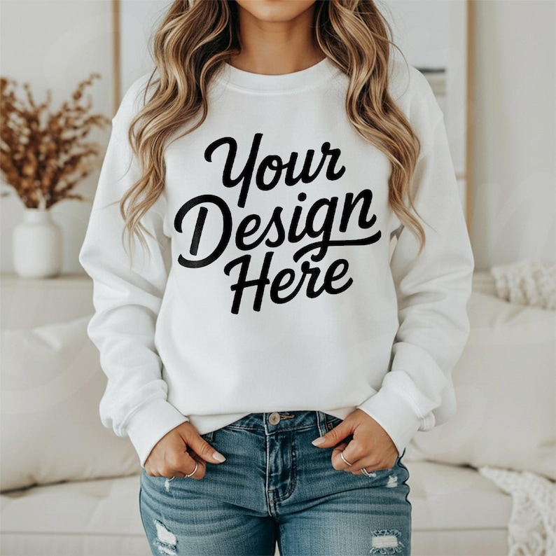 May include: White crew neck sweatshirt with the text "Your Design Here" in black script. The sweatshirt is being worn with blue jeans. The image is a mockup for a clothing design.