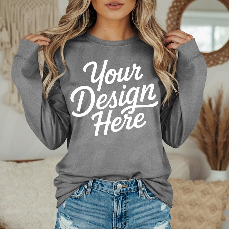 May include: A gray long-sleeve sweatshirt with the text "Your Design Here" in white script. The sweatshirt is paired with denim shorts. The image is a product mockup, ideal for showcasing custom designs.
