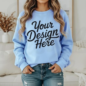 May include: A light blue sweatshirt with the text "Your Design Here" in black script. The sweatshirt has long sleeves and a crew neck. The model is wearing blue jeans.