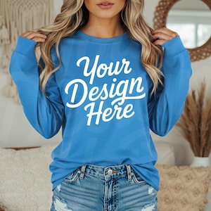 May include: A long-sleeved, blue shirt with the text "Your Design Here" in white script. The shirt is a solid color and appears to be made of a soft material. The model is wearing denim shorts.