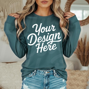 May include: Teal long-sleeve shirt with the text "Your Design Here" in white script. The shirt is paired with denim shorts. The image is a mockup, likely for showcasing custom designs on apparel.