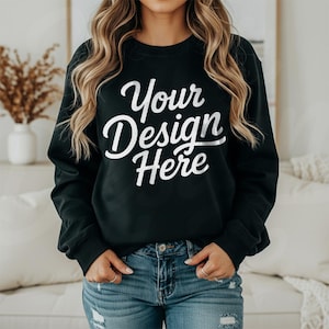 May include: Black crew neck sweatshirt with the text "Your Design Here" in white script. The model is wearing blue jeans. The sweatshirt is a solid color and has long sleeves.