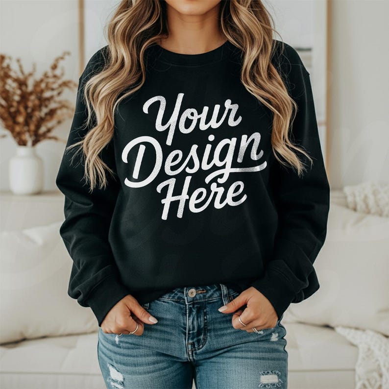 May include: Black crew neck sweatshirt with the text "Your Design Here" in white script. The model is wearing blue jeans. The sweatshirt is a solid color and has long sleeves.