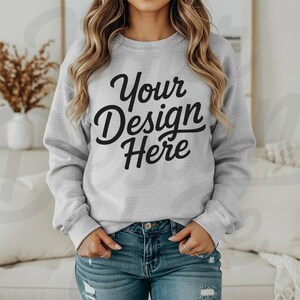 May include: A light gray sweatshirt with the text "Your Design Here" in black script. The model is wearing blue jeans. The sweatshirt is a crew neck style.